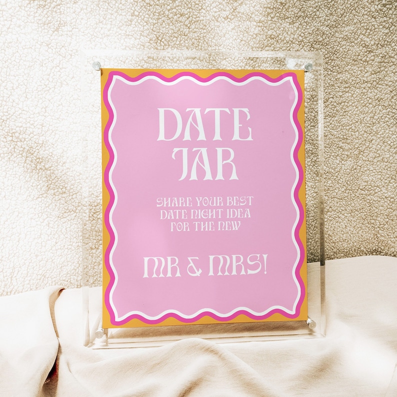 May include: A pink and gold sign with the text "DATE JAR" and "SHARE YOUR BEST DATE NIGHT IDEA FOR THE NEW MR & MRS!" in white lettering.