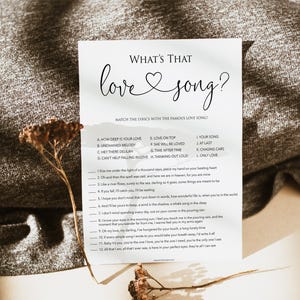 May include: A printable game card with the title "What's That Love Song?" and a list of song titles and lyrics to match. The card has a white background with black text and a heart symbol.