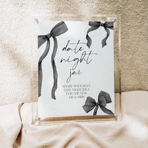May include: A white sign with black text and gray watercolor bows that reads "date night jar" and "SHARE YOUR BEST DATE NIGHT IDEA FOR THE NEW MR & MRS!"