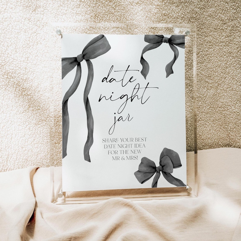 May include: A white sign with black text and gray watercolor bows that reads "date night jar" and "SHARE YOUR BEST DATE NIGHT IDEA FOR THE NEW MR & MRS!"