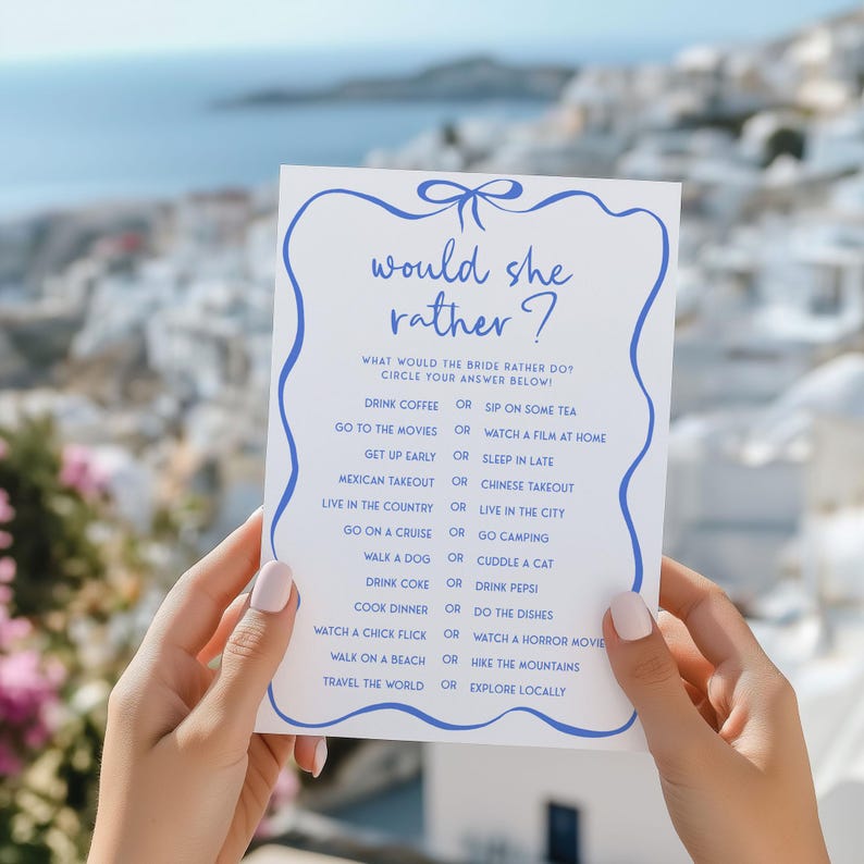 May include: A white card with blue text and a blue bow at the top. The card has the text "would she rather?" and a list of questions with two options each. The questions are about the bride's preferences, such as "Drink coffee or sip on some tea?" and "Go to the movies or watch a film at home?"