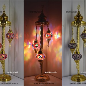 May include: A gold floor lamp with three hanging mosaic glass globes. The globes are lit and cast colourful light. The lamp has a gold base and a gold chain.