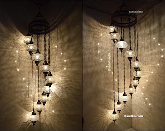 May include: A spiral chandelier with multiple clear glass globes hanging from a central metal frame. The chandelier is lit and casts a warm glow on the surrounding wall.