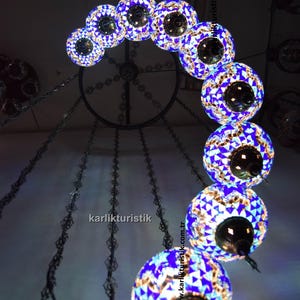 May include: A decorative chandelier with multiple mosaic glass globe lights. The globes are primarily blue and white, with a mosaic pattern. The chandelier is suspended from the ceiling by chains. The text "@karlikturistik" is visible.