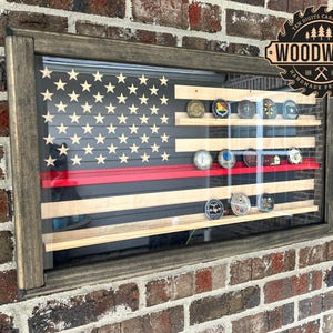 May include: A wooden shadow box with a red, white, and blue American flag design. The shadow box has multiple shelves for displaying coins or other small items. The shadow box is mounted on a brick wall. The text "Ten Digits Carpentry WOODWORK Handmade Products" is visible in the upper right corner of the image.