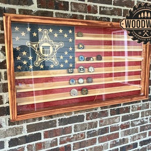 May include: A wooden shadow box with a red, white, and blue American flag design. The shadow box has glass on the front and is displaying a collection of challenge coins. The shadow box is mounted on a brick wall. The text "Ten Digits Carpentry Woodwork Handmade Products" is on a circular label in the upper right corner of the image.