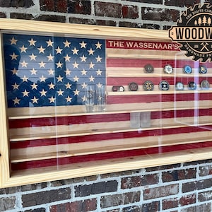 May include: A wooden American flag shadow box display with glass front and shelves for displaying military challenge coins. The shadow box is labeled "The Wassenaar's" and has a woodburned logo for "Ten Digits Carpentry Woodwork Handmade Products".