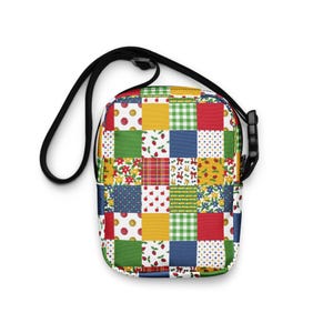 May include: A colorful crossbody bag with a patchwork design. The bag features a black adjustable strap and a rectangular body composed of various patterned squares in red, yellow, green, and blue. The patterns include floral, polka dots, and gingham.