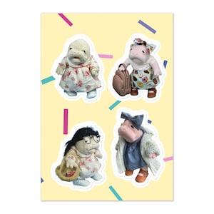 May include: Four plush toy hippos wearing different outfits. One hippo is wearing a white dress with pink flowers, another is wearing a blue dress with a white cardigan, another is wearing a blue and white dress with a brown bag, and the last hippo is wearing a pink and white dress with a brown bag.