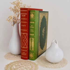 Puede incluir: Dos libros antiguos de tapa dura con detalles dorados y lomos decorativos. El libro de la izquierda es rojo y dice "Bernard Shaw Plays" y "The Franklin Library". El libro de la derecha es verde y dice "My Antonia Willa Cather".