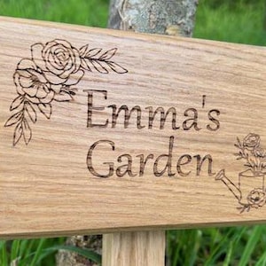 May include: A wooden sign with the text "Emma's Garden" engraved on it. The sign is decorated with a floral design and a watering can.
