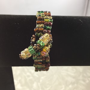 May include: A beaded bracelet with a knot design. The beads are in shades of brown, green, and gold.
