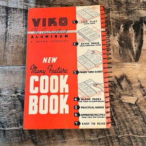 May include: A vintage cookbook titled "VIKO Cook Book" with a red cover and white lettering. The cover features the text "The Guaranteed Aluminum" and "A Mirro Product." The cookbook is spiral-bound and includes features like blank pages and practical menus.