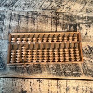 May include: A wooden abacus with brown beads and a wooden frame. The abacus has 13 rows of beads, with 5 beads per row. The abacus is a traditional counting tool used in many cultures.