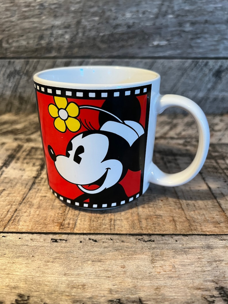May include: White ceramic mug featuring a red, black and yellow image of Minnie Mouse. The image is framed with a black and white film strip design.