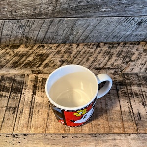 May include: White ceramic mug with a black, red and white design featuring a cartoon image of Minnie Mouse. The mug has a black handle.