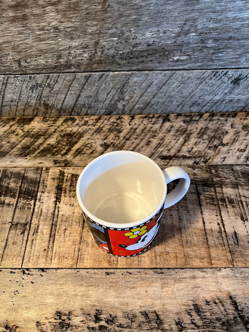 May include: White ceramic mug with a black, red and white design featuring a cartoon image of Minnie Mouse. The mug has a black handle.
