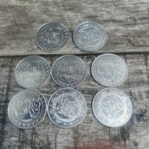 May include: A collection of silver-colored, round tokens with embossed designs. The tokens feature the text "Soho Snack" and other text. The tokens are arranged on a weathered wooden surface.