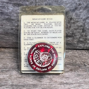 May include: A red and white Milkcap game piece with the text "Explore the Wonder of Nature at Earth Home" around a fossil design. The game piece is in a clear plastic package with game rules.