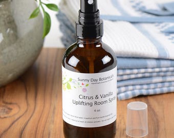 May include: A brown glass bottle with a black spray nozzle filled with citrus and vanilla uplifting room spray. The bottle is labeled "Sunny Day Botanicals Handmade Essential Oil Blends Citrus & Vanilla Uplifting Room Spray 4 oz."