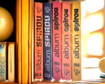 May include: A collection of colorful "album Spirou" comic books, with spines in orange, blue, pink, and yellow. Each book features the title and a number, with a cartoon character illustration. The books are arranged on a wooden shelf.