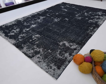 May include: A dark blue rug with a distressed, faded look. The rug has a white and gray pattern throughout. The rug is lying on a white surface with a basket of colorful yarn balls in the lower right corner.