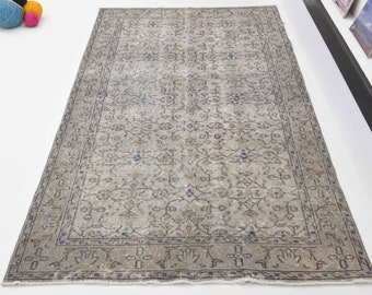 May include: A vintage rug with a faded floral pattern in shades of gray and blue. The rug has a distressed look and a fringed edge.