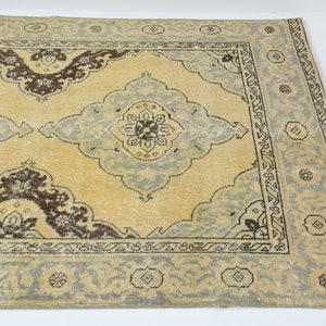 Puede incluir: Una alfombra vintage con un fondo beige claro y un diseño central de medallón. El medallón presenta un patrón floral azul claro y marrón. La alfombra tiene un borde con un patrón geométrico azul claro y marrón.
