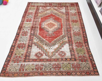 Könnte beinhalten: Ein Vintage-Teppich in Rot, Weiß und Beige mit einem zentralen Diamantenmuster und einem komplizierten floralen Rand. Der Teppich hat einen abgenutzten, verblassten Look, der ihm einen einzigartigen Charakter verleiht.