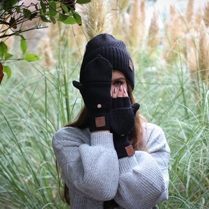 Może przedstawiać: Osoba w czarnej wełnianej czapce i dopasowanych bezpalcowych rękawiczkach. Rękawiczki mają brązową skórzaną naszywkę z logo po obu stronach.