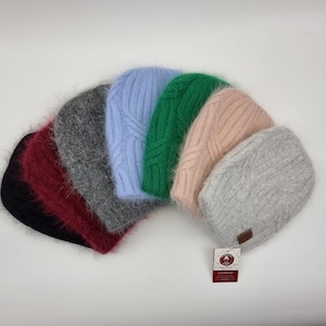 May include: A collection of six fuzzy knit hats in various colors, including black, burgundy, gray, light blue, green, and pink. The hats are arranged in a semi-circle and have a cable knit pattern. The tag reads "CASHMERE".