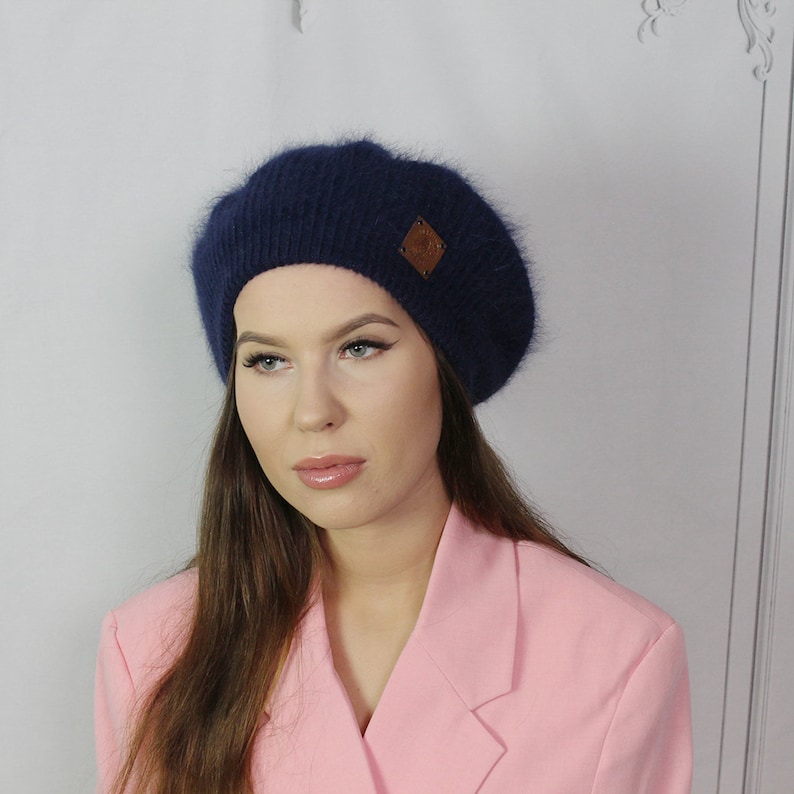 May include: A navy blue beret with a brown leather patch. The beret is made of a soft, fuzzy material.