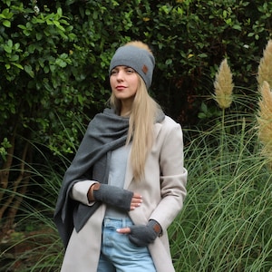 May include: A gray knit beanie with a faux fur pom pom, a gray scarf, and gray fingerless gloves. The beanie has a brown leather patch on the side.