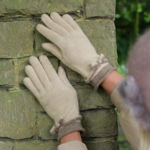 Peut inclure: Une paire de gants en tricot crème avec un poignet marron contrastant et un petit nœud décoratif. Ces gants sont fabriqués dans une matière douce et chaude. Accessoire élégant pour l'hiver.
