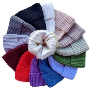 Puede incluir: Una colección de gorros de punto de colores, incluyendo rojo, azul, verde y gris, dispuestos en un patrón circular. Una scrunchie de satén blanco está en el centro. Los gorros tienen una textura acanalada y puños doblados.