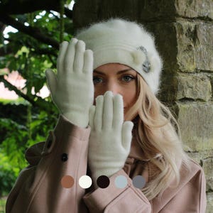 May include: Cream-coloured gloves and a matching beret with a decorative embellishment. The gloves are made of a soft, knitted material. The beret has a small, decorative pin. The coat is a light brown colour.