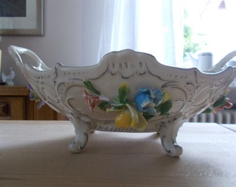 Może przedstawiać: Biała porcelana z ozdobnymi detalami i trzema nóżkami. Miska jest ozdobiona kolorowymi kwiatami i liśćmi.