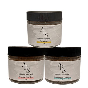 Puede incluir: Tres frascos de vidrio con exfoliante de azúcar moreno. Los frascos tienen tapas negras y etiquetas blancas con el texto "ARS" en negro. Las etiquetas también incluyen el texto "Exfoliating Sugar Scrub" y el aroma de cada exfoliante: "Citrus Glow", "Energize Your Day" y "Harmonizing Eucalyptus".
