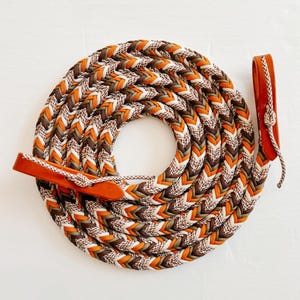 May include: A braided leather horse rein with a chevron pattern in brown, orange, and white.