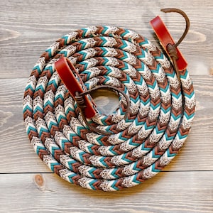 May include: A coiled rope with a braided pattern in brown, teal, and white. The rope has leather accents in a reddish-brown color. The rope is designed for equestrian use.