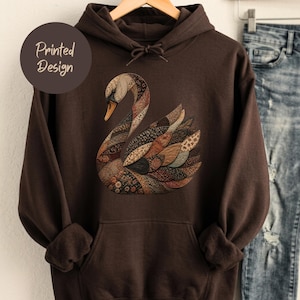 May include: A dark brown hooded sweatshirt featuring a central graphic of a swan composed of various patterned fabric-like textures in shades of brown, tan, and orange. The text Printed Design appears in a circular badge on the upper left side.