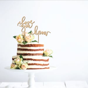 May include: A two-tiered cake decorated with fresh flowers and a wooden cake topper that reads "love you know".