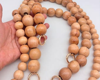 May include: A long wooden bead chain with gold clasps. The beads are natural wood and have a light brown color.