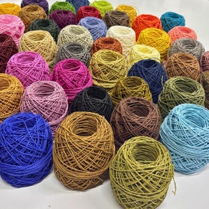 May include: A collection of colorful yarn balls in various shades of blue, green, brown, pink, red, and yellow. The yarn balls are arranged in a circular pattern on a white surface.