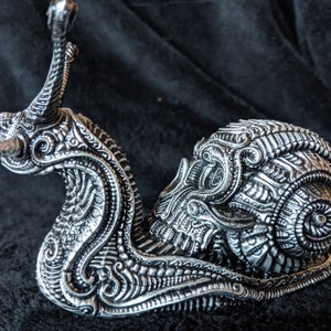 May include: A silver snail sculpture with intricate details and a curled shell. The snail is made of metal and has a highly detailed, ornate design.