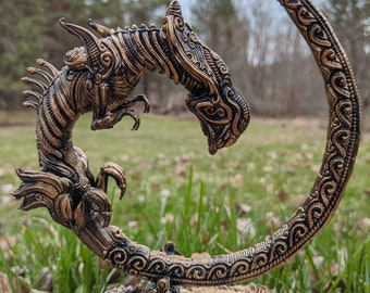 May include: A gold-colored metal dragon sculpture with intricate details. The dragon is curled in a circle, with its head facing the viewer. The sculpture is on a wooden base.