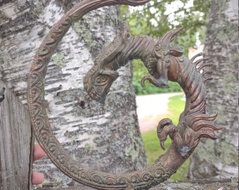 May include: A bronze dragon sculpture with intricate details, curled in a circle with its tail in its mouth. The sculpture has a green patina and is mounted on a base with three legs.