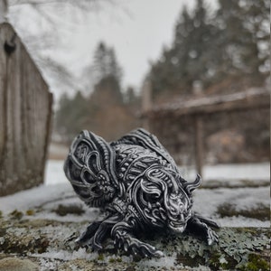 May include: A detailed, silver-colored, insect-like sculpture with intricate wings and a textured surface. The sculpture is posed on a wooden log covered in moss and snow.