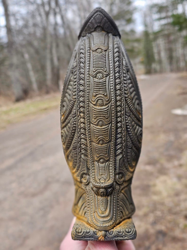 May include: A dark grey ceramic sculpture with intricate patterns and designs. The sculpture is shaped like a bird with a long, pointed beak and a rounded body.