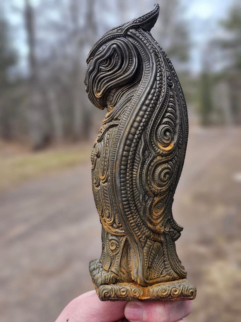 May include: A detailed, intricately carved, dark grey and brown statue of a mythical creature with a long, flowing mane. The statue is made of a textured material and has a base with a decorative design.